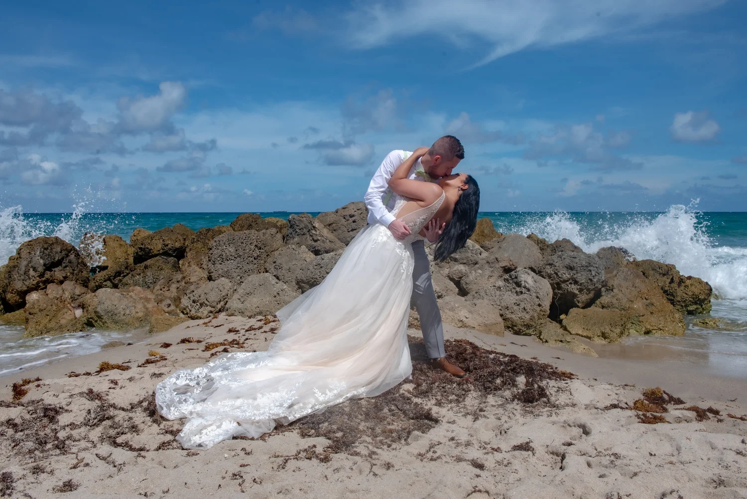 Wedding couple sharing a dip kiss beside rocks and ocean water in South Florida